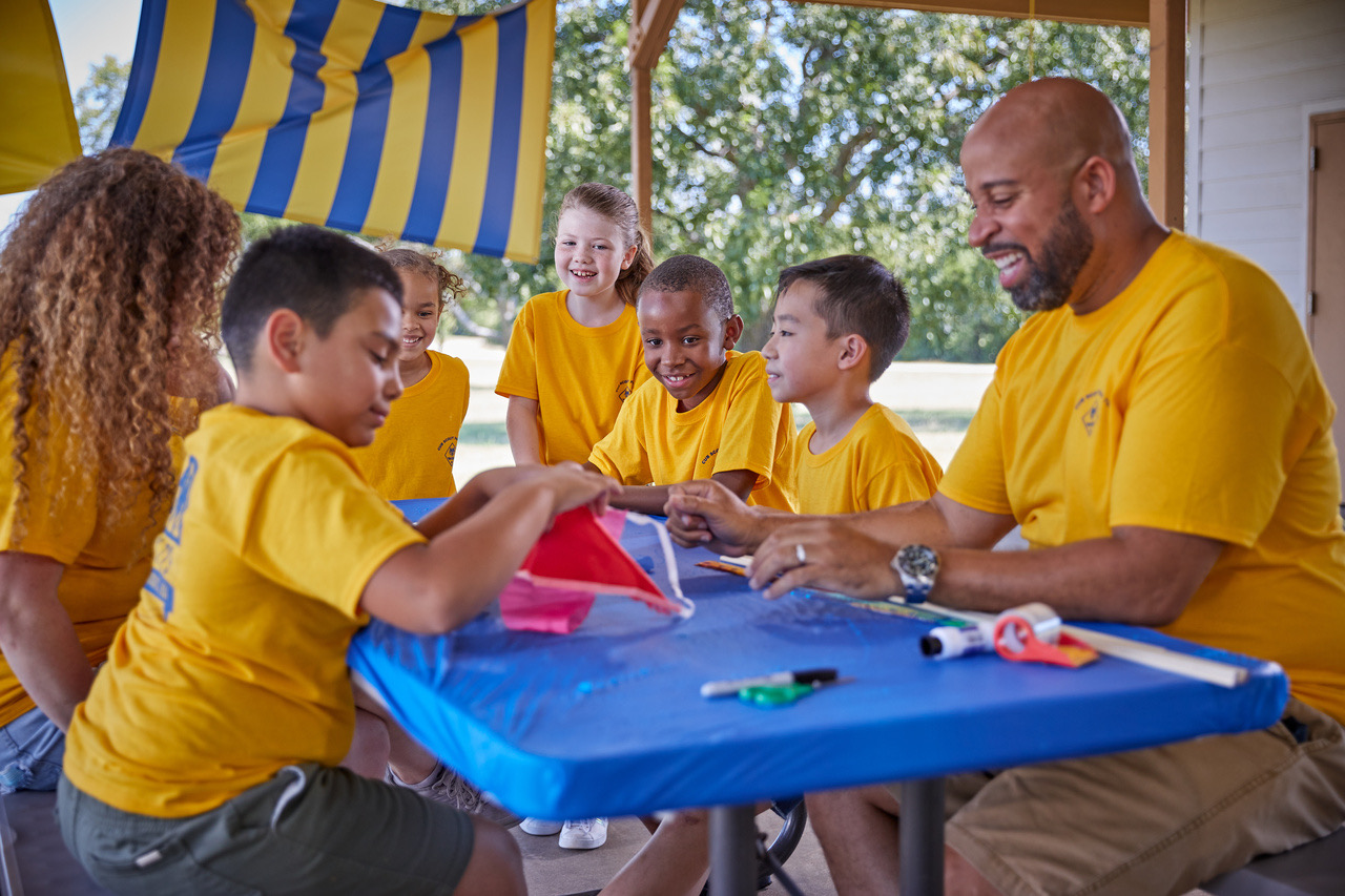 Cub Scouts and a leader working on a project together around a table at a den meeting