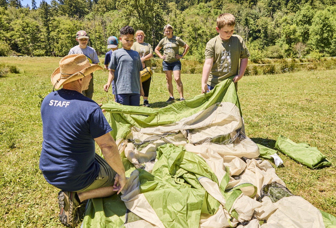 Cub Scouts and adult leaders setting up a tent in a meadow