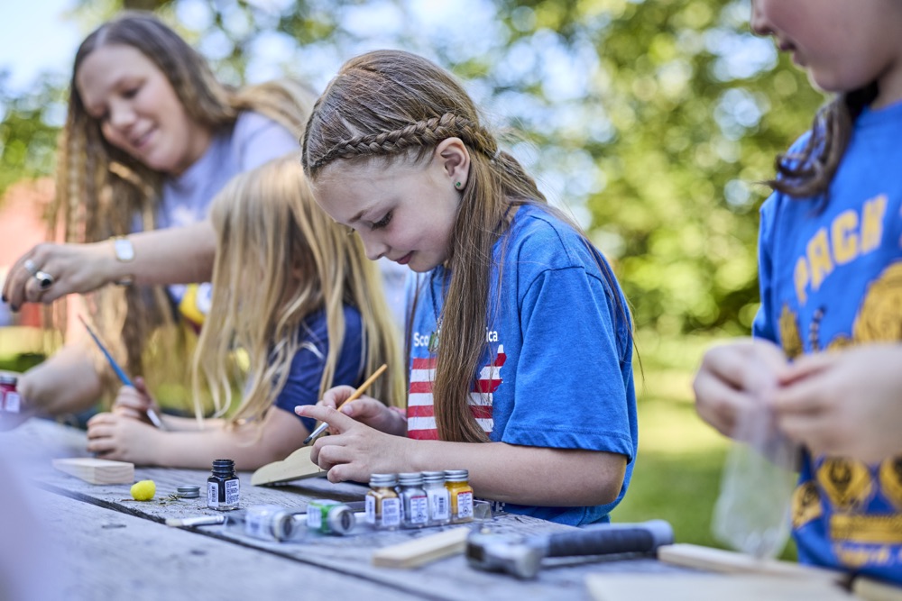 A Cub Scout painting a pinewood derby car at a workbench